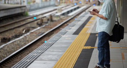 駅のホームで携帯電話を見ながら電車待ちの中年男性 - obrazy, fototapety, plakaty
