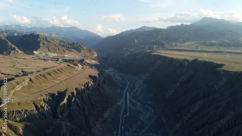 Poster Drone footage over dry river under green hills with rural houses with cloudy sky