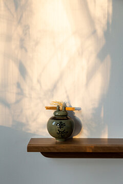 Small round green ceramic urn with Chinese characters on shelf set against wall with tree branches shadows