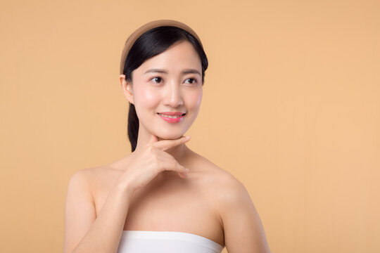 Beautiful girl asian model touching fresh glowing hydrated facial skin on beige background closeup. Beauty face young woman with natural makeup and healthy skin portrait. Skin care concept