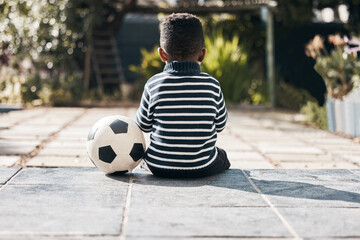 Sitting, back and a child in yard with a ball for soccer, playing and childhood game. Training, sports and a little boy kid with a football for exercise, waiting and exercise in a backyard on weekend - Powered by Adobe