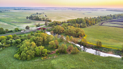 Spring morning landscape. Railroad bridge crossing calm river in blooming meadows. Aerial rural view from above. Agricultural yellow green colza fields. Dandelion blossom scene. - 606001290