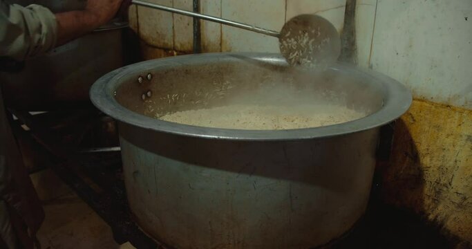 Slow motion of a chef stirring on a cauldron of rice in a restaurant