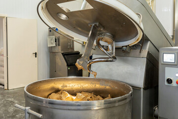 An industrial machine for mixing dough in a bakery. The upper part of the mixer is raised, the...