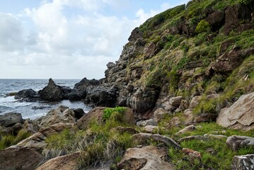 Beautiful shot of blue seawater near a rocky seashore with green cliffs