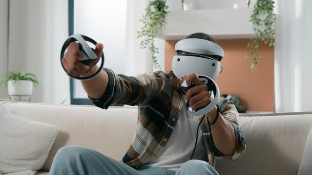 African American man having fun at home couch with virtual reality video game fight guy play 3d cyber gaming fighting with controllers man playing in VR glasses helmet using joysticks metaverse world