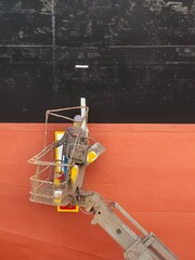 A shipyard worker on a cherry picker is painting on a ship side