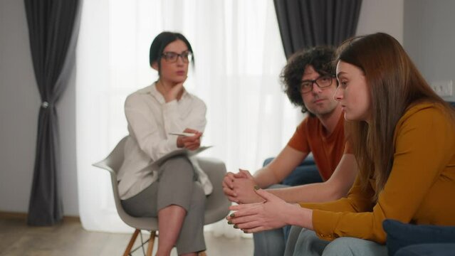 Couple having therapy session with a psychologist to solve their relationship problems and crisis. Sad man covering his ears with hands to avoid hearing abuse