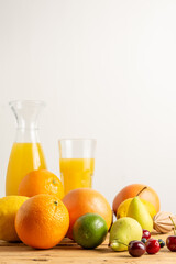 Close up of oranges, grapefruits, cherries and pears on wooden table with bottle and glass of orange juice, white background, vertical, with copy space