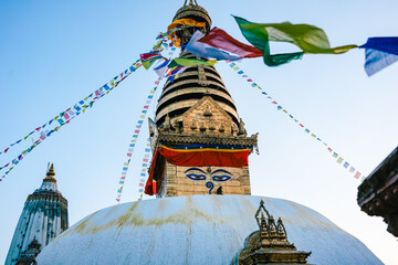 View of the golden top of the Swayambhu Stupa in Kathamndu Nepal. Colorful prayer flags wave against a blue sky