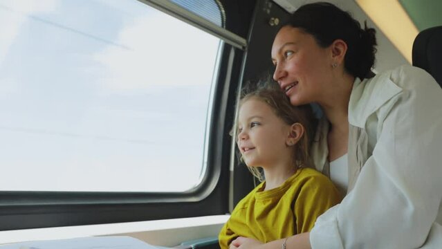 Mother and daughter traveling by train sitting by the window, traveling with a child on a high-speed train in the summer