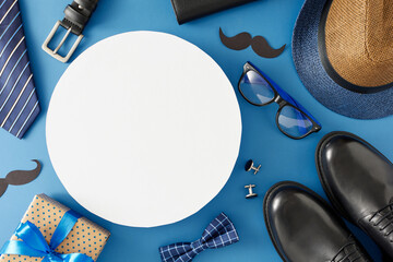 Happy Father's Day concept. Top view flat lay of gift box, dad's leather shoes, mustache, men's accessories and hearts on blue background with blank circle for text or promotion