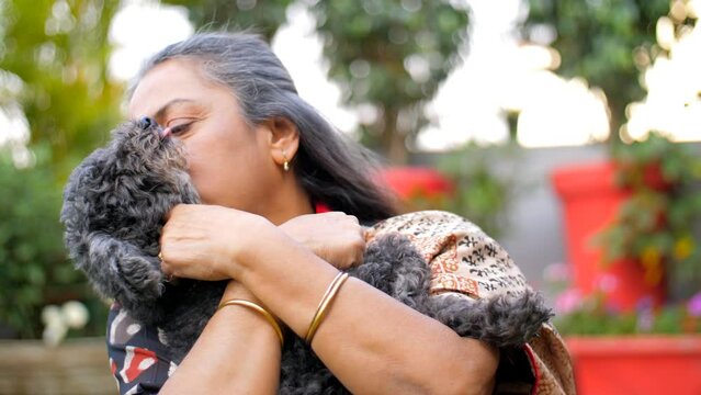 A middle-aged Indian woman is hugging/cuddling a black dog - a domestic animal  ornamental dog. An Indian housewife in a Saree is relaxing with her pet dog in the garden - love and affection  leisu...