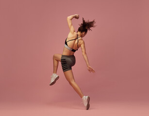 Obraz na płótnie Canvas Full-body workout. Dynamic image of young sportive woman in sportswear training, posing in motion against pink studio background. Concept of sportive lifestyle, beauty, body care, fitness, health