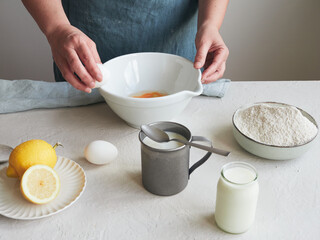 woman's hands with egg on a bowl to mix ingredients and prepare a dessert or pastry recipe. Flour, milk and lemon on the table.