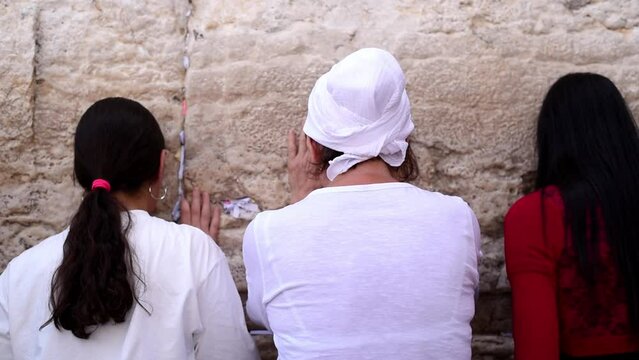 Three women standing and praying on Western Wall with notes of paper containing written prayers placing in cracks and crevices. Wall old part of Jerusalem city. tourism, travel and vacation to Israel
