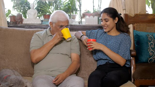 A cheerful old gentleman and his adult daughter spend quality time - in casual conversation - bonding and care. An Indian father-daughter duo are enjoying while drinking a cup of tea/coffee togethe...