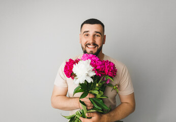 image of a handsome man with a bouquet of pink peonies as a gift. Smiling man with flowers, isolated on a gray background.