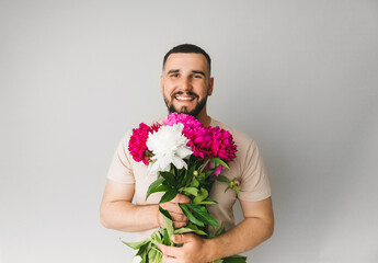 image of a handsome man with a bouquet of pink peonies as a gift. Smiling man with flowers, isolated on a gray background.