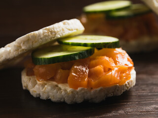 Close-up, macro, sandwich with two pieces of crispy rice bread, cucumber, butter and salted salmon on dark rustic wooden background