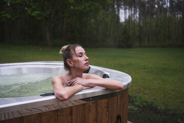 Young happy woman relaxing in hot tub. Enjoying welness SPA outside in the forests. Hot bath SPA