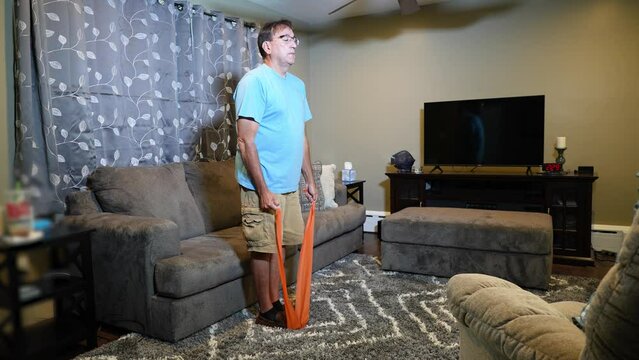 A man using an exercise fitness band at home. The band slips off and slaps him in the face.  	