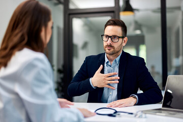 A man touches his chest and complains of very strong pain to a female doctor.