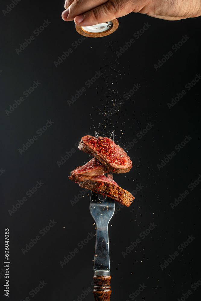 Wall mural Grilled meat steak and adding seasoning, Fresh raw Prime Black Angus beef steak on a fork