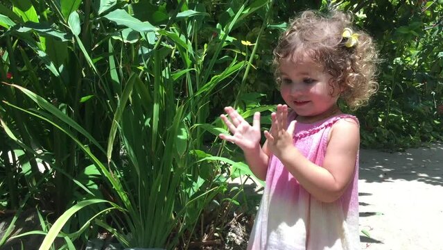 Little girl in pink summer dress and curly hair walking in beautiful park with butterflies, discovering nature and wild life. High quality FullHD footage