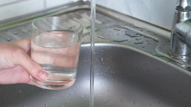Caucasian woman hand holding a glass with pure drinking water pouring from home faucet close up