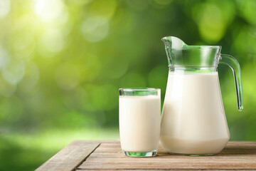 Glass and pitcher of fresh milk on wooden table with blur green garden background.