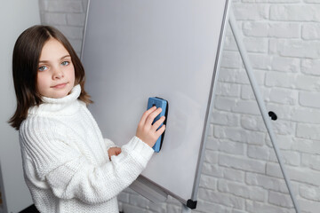 Little girl standing and cleaning whiteboard. Child smiling and looking at camera