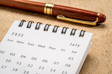 July 2023 - closeup of a small desktop calendar with a pen, time and business concept