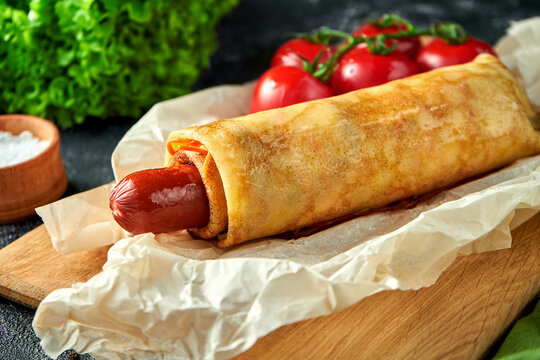 Hot dog with sauce on parchment on a dark background. Sausage wrapped in crepe
