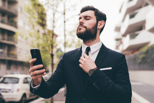 Young bearded elegant businessman outdoors doing videocall using smartphone