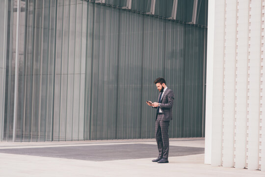Young bearded elegant businessman outdoors using smartphone