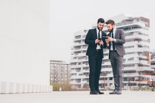 Two young contemporary businessman outdoor in the city using smart phone