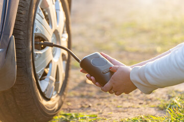 A woman's hand holds a wireless portable air pump for inflating car tires
