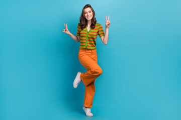 Full size photo of satisfied cheerful woman dressed orange pants colorful cardigan showing v-sign isolated on blue color background