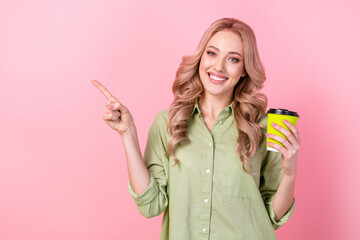 Photo of shiny pretty woman dressed green shirt drinking coffee pointing empty space isolated pink color background