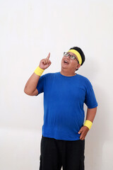Asian overweight man in sportswear standing while pointing above. Isolated on white