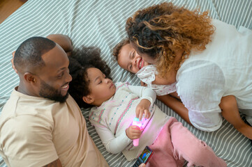 Happy African American Parents with  little daughters playing on the bed in bedroom at home, happy family concept