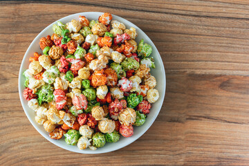 A rainbow of sweet popcorn in a plate on a wooden background