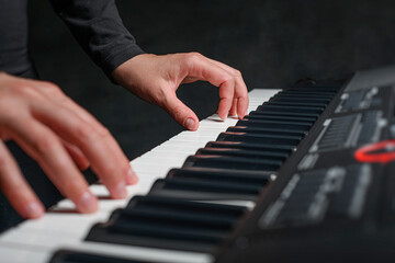 Playing a synthesizer on a dark background. The musician plays the synthesizer.