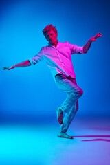 Fototapeta na wymiar Full-length portrait of mature man in white shirt and checkered pants dancing against blue studio background in pink neon light. Concept of human emotions, lifestyle, youth, facial expression