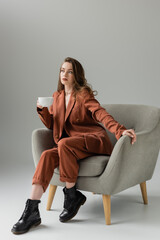 brunette young woman with long hair and necklace wearing terracotta and trendy suit with blazer and...