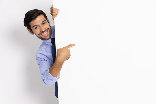 Young businessman pointing and standing behind the white blank banner or empty copy space advertisement board on white background, Looking at camera