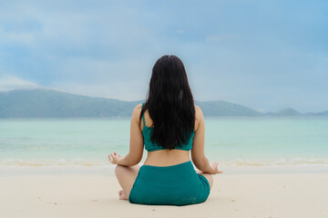 Fototapeta na wymiar Woman meditating in lotus yoga on coast of sea on the beach. Peaceful healthy and fit young woman meditating on the beach. Woman practicing yoga by the sea
