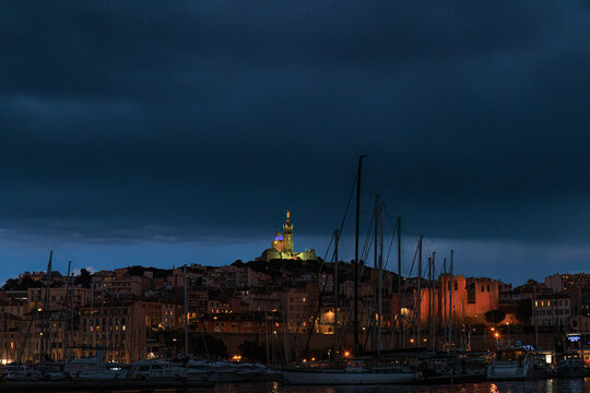 A scenics view of the city of Marseille, bouches-du-rh&ocirc;ne, France at night with the old port in the with boats and the illuminated basilique notre-dame-de-la-garde (la bonne m&egrave;re)