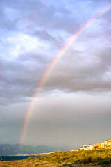 Vertical image of rustic coastline with rainbow and dark blue horizon